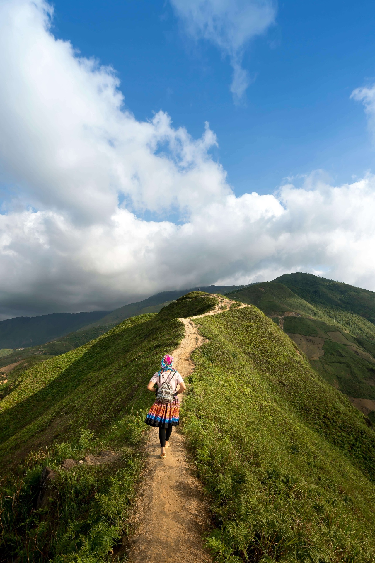 Donna in costume tradizionale Hmong cammina su un sentiero tra le montagne verdi del Vietnam — viaggio lento a contatto con la natura